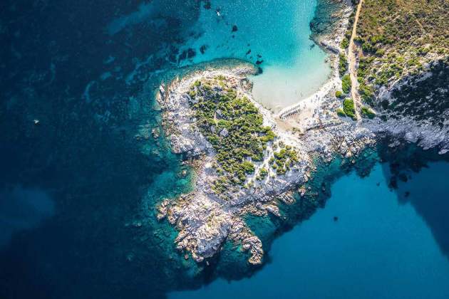 Ein Blick aus Vogelperspektive über ein türkises Meer und eine Insel mit weißem Sand und Büschen