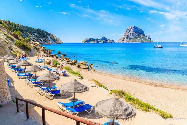 Cala d'Hort Strand mit Sonnenschirmen und einem bluen Meer.
