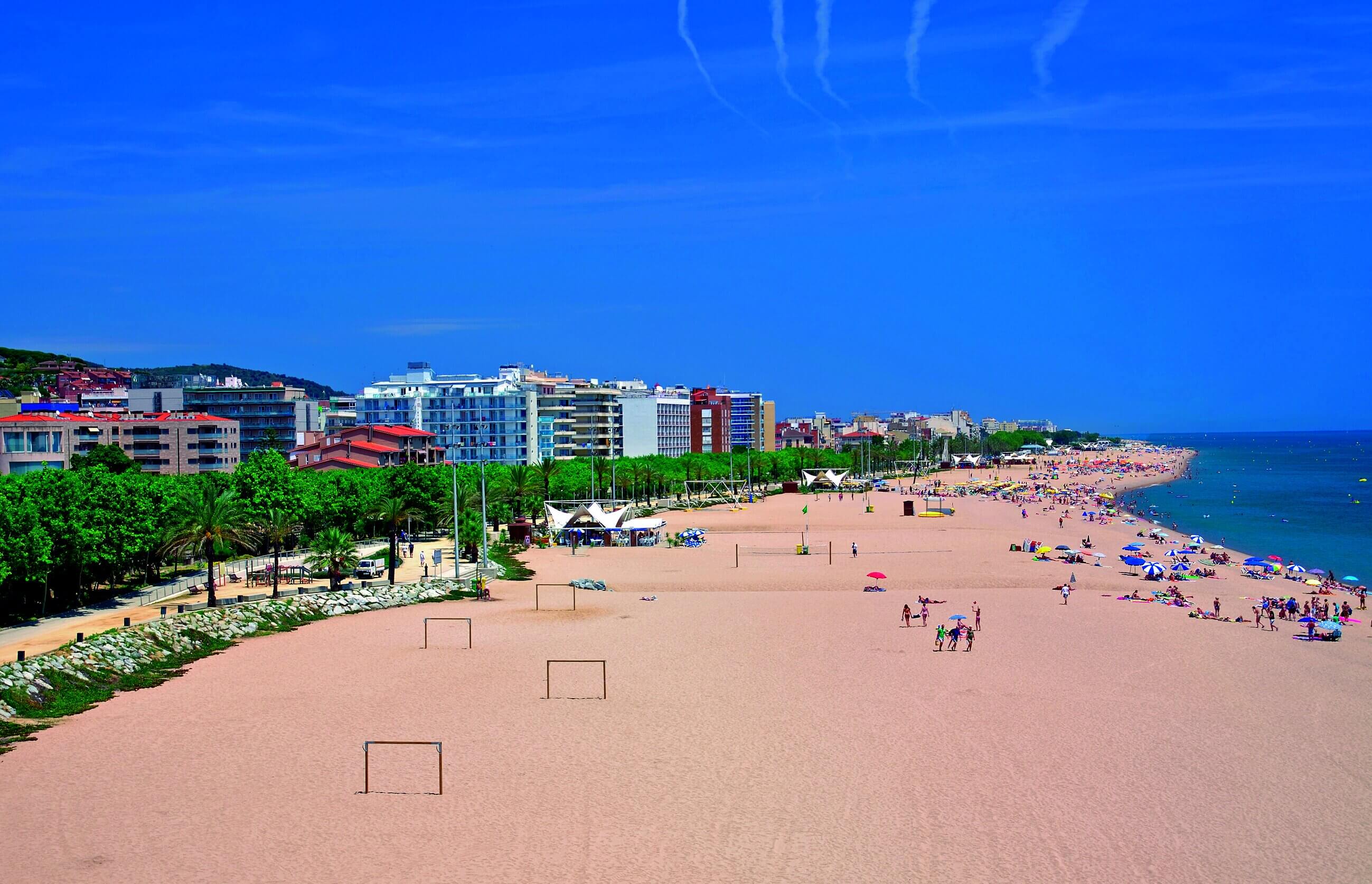 Ein breiter Sandstrand mit vielen Badegästen. Im Hintergrund sind Hotels.