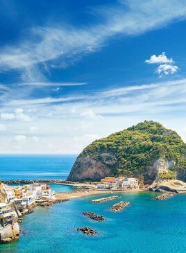 Riesiger Felsen in der Nähe des kleinen Dorfes Sant'Angelo auf der Insel Ischia, Italien Ein Riesiger Felsen mit Bäumen umgeben von Türkisem Meer