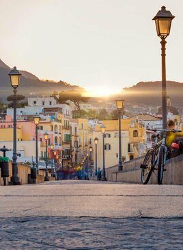 Blick auf den Sonnenuntergang aus der Ischia Straße mit bunten Häusern, Italien Blick von einer Brücke auf die Stadt beim Sonnenuntergang. Auf der Brücke sind historische Laternen.