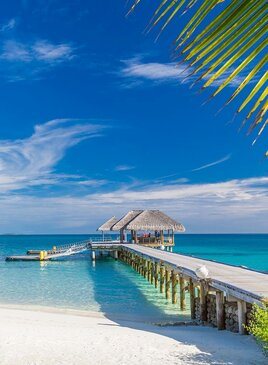 Eine hölzerne Brücke führt zu einer Pergola über dem Wasser.