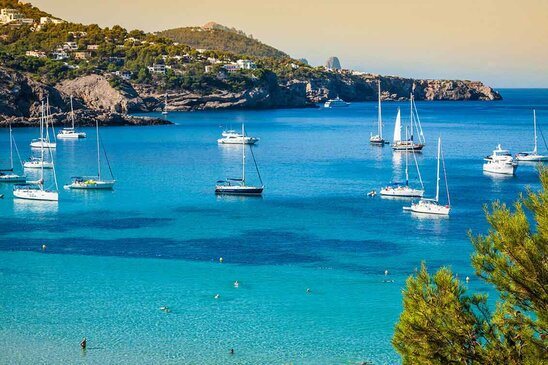 Cala Tarida in Ibiza beach San Jose at Balearic Islands Schiffe auf einem blauen Meer. Im Hintergrund ist die Stadt San José.