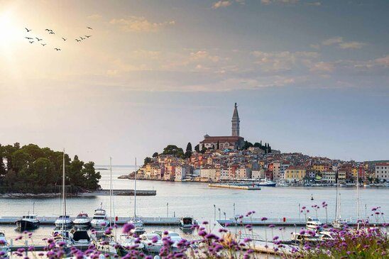 Ausblick auf die Stadt Roving mit vielen Häusern beim Sonnenuntergang mit Schiffen im Vordergrund