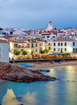 Viele weisse häuser hinter einem Strand. Im Hintergrund ragt ein Turm hervor.