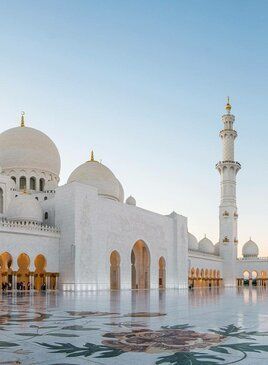 Die Scheich-Zayid-Moschee aus weissem Stein mit einer großen Pforte, einem Turm und Kuppeln