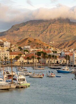 Ein Hafen mit vielen Schiffen. Im Hintergrund sind von Wolken bedeckte Berge.