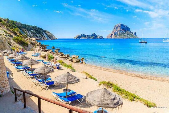 Cala d'Hort Strand mit Sonnenschirmen und einem bluen Meer.