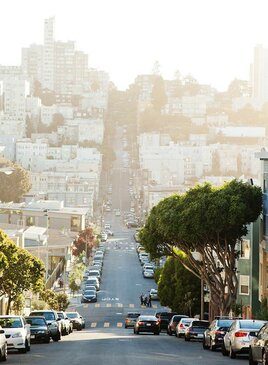 Eine lange Straße mit Autos auf beiden Seiten und verschiedenen Wohnhäusern.