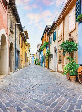 Eine gepflasterte Gasse in San Guiliano mit farbenfrohen Häusern und Pflanzen. 