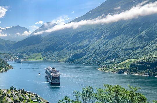 Ein Kreuzfahrschiff fährt zwischen Bergen und einer Stadt um anzulegen
