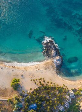 Ein Sandstrand aus Vogelperspektive. Auf der obere Hälfte des Bilder ist ein türkises Meer.