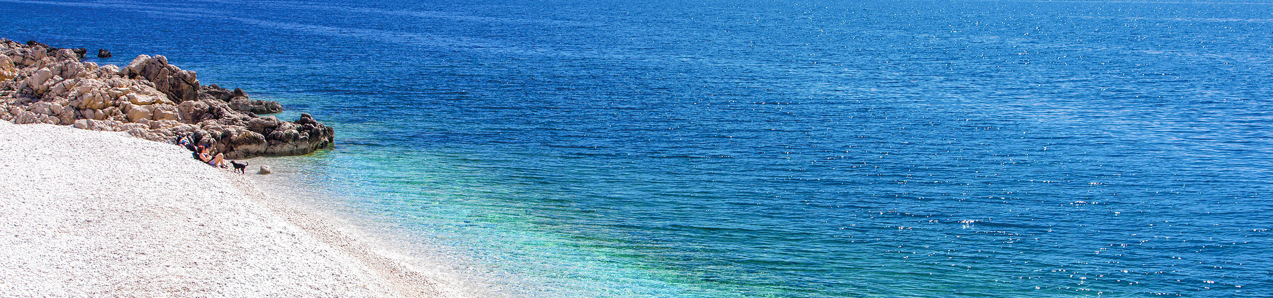 Feiner Kiesestrand im Hintergrund das azurblaue Meer.